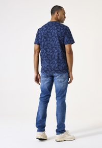 Camiseta navy con un patrón de hojas, de mangas cortas; combinada con jeans de color azul claro y zapatillas beige; mostrada desde la parte de atrás.