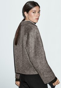 Brown wool-blend jacket with a relaxed fit, wide sleeves, and contrasting black cuffs. Smooth texture and minimalistic design.