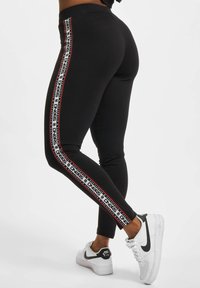 Sorte leggings med sidestriper og hvit og rød merkevare. Kombinert med hvite joggesko. Glatt tekstur og tettsittende design.
