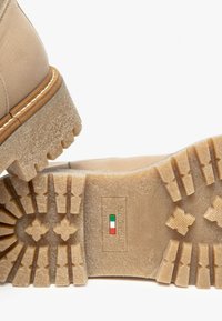 Stivale alla caviglia in pelle beige con suola in gomma testurizzata, caratterizzato da un motivo di battistrada spesso e da un'etichetta con i colori della bandiera italiana.