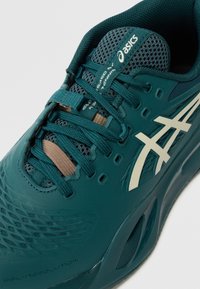 Türkisfarbene Sportschuhe mit Netzobermaterial, Schnürsystem und hellbraunen Akzenten. Verfügt über eine strukturierte Oberfläche und ein markiertes Logo an der Seite.