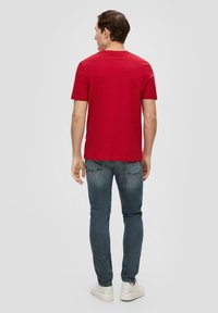 Rode katoenen T-shirt met korte mouwen, ronde hals, en een losse pasvorm, gecombineerd met slim-fit denim jeans en witte sneakers.