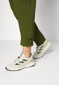 Lätta idrottsskor i krämfärg med svarta accenter. Har ett andningsbart ovandel i mesh, elastiska snören och en texturerad gummisula.