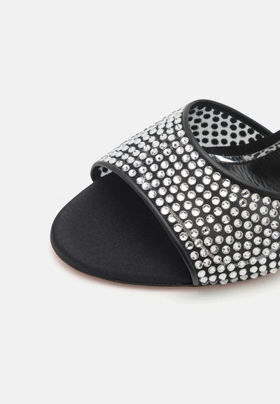 Black sandal featuring a wide strap adorned with silver rhinestones and a smooth, matte black toe area. Textured inner lining visible.