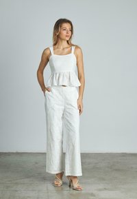 Top peplum bianco ricamato con fiori, con scollatura quadrata, abbinato a pantaloni bianchi a gamba larga. La modella indossa tacchi beige con fasce.