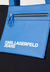 Blå fodrad läderpouch med dragkedja, med vit logotext "KARL LAGERFELD JEANS" och en kontrasterande svart tygbakgrund.