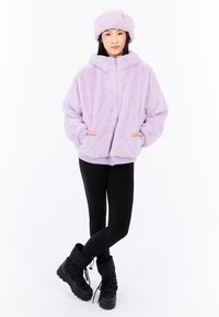 Laventelin värinen ylisuuri fleece-takki huppuineen, jossa on vetoketjusuljenta ja taskut. Yhdistetty mustiin leggingseihin ja tikkukorkeisiin mustiin saappaisiin.