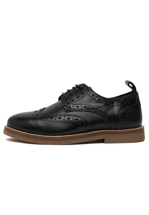 Zapato brogue de cuero negro con detalles de ala, perforaciones, cierre de cordones y suela de goma color canela.