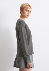 Szürke kötött pulóver hosszú ujjal, bordázott aljjal és puha textúrával, egy farmer mini szoknyával párosítva, oldalnézetből.