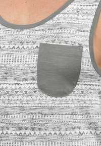 Grå mønstret tanktop med rund hals og en matchende brystlomme, med geometriske design i svart på hvit bakgrunn.