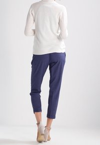 Suéter ajustado gris claro con dobladillo y puños acanalados, combinado con pantalones estrechos azul marino y sandalias de tacón alto beige. Diseño simple y moderno.