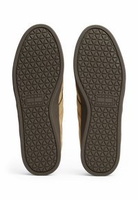 Beige Wildlederschuhe mit einer strukturierten Gummisohle, die ein Diamantmuster aufweist, und einem Markenlabel "TOMMY JEANS" nahe dem Rand.
