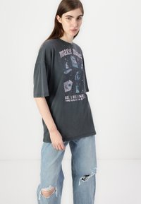 T-shirt en coton oversize noir avec des textes graphiques colorés et des illustrations. Associé à un jean en denim bleu clair déchiré.