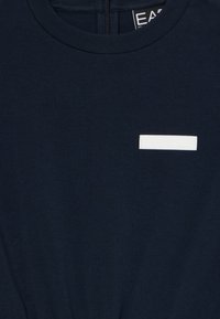 Ναυτικό μπλε βαμβακερό t-shirt με στρογγυλή λαιμόκοψη και μικρή λευκή ορθογώνια λογότυπο επένδυση στο στήθος. Μαλακή, λείες υφή.