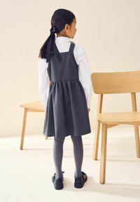 Grijze denim jurk met een geraffineerde taille, wit overhemd, grijze maillot en zwarte schoenen. Eenvoudig ontwerp met een zwarte strik in het haar.