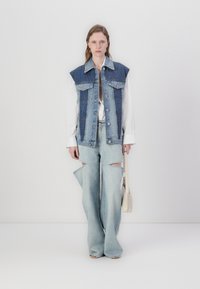 Denim vest with oversized shoulders, blue color and button closures. Flared light blue jeans featuring side cutouts. Minimalist handbag.