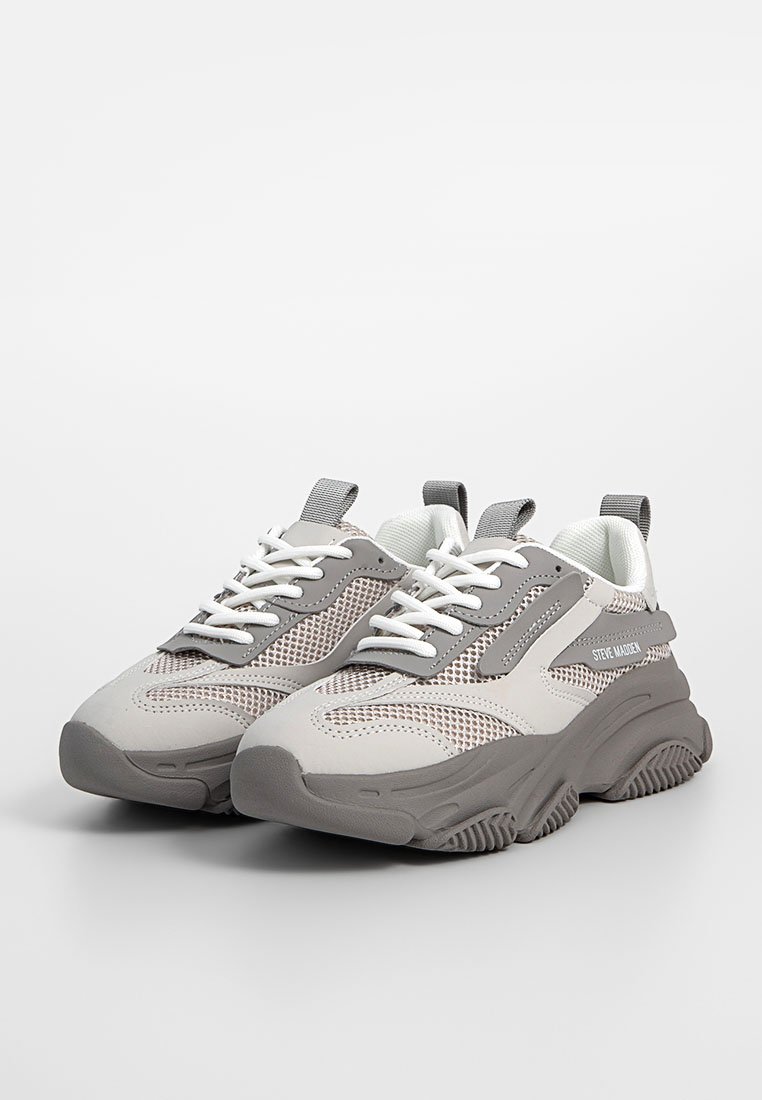 Grå och vit sneaker med ovandel i mesh, tjock gummisula och texturerade detaljer. Snören och logotypdetalj finns på sidan.