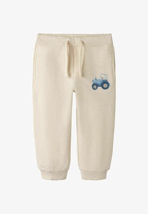 Beige peuter joggingbroek met trekkoord in de taille, geribbelde enkels, zijzakken en een kleine blauwe tractorafbeelding op het rechterbeen.