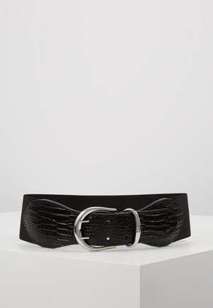 Ceinture large noire en cuir synthétique effet crocodile texturé avec une grande boucle double ardillon argentée, posée sur une surface blanche unie.