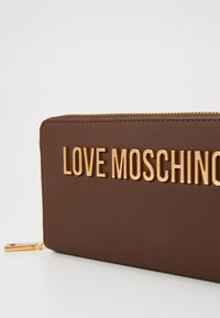 Rudas dirbtinės odos piniginė su auksiniu "LOVE MOSCHINO" užrašu priekiniame šone. Yra su užtrauktuku ir glotnia tekstūra.