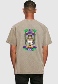 Beige cotton t-shirt featuring a colorful graphic of a woman in a white dress with a paint palette, surrounded by leaves and text.