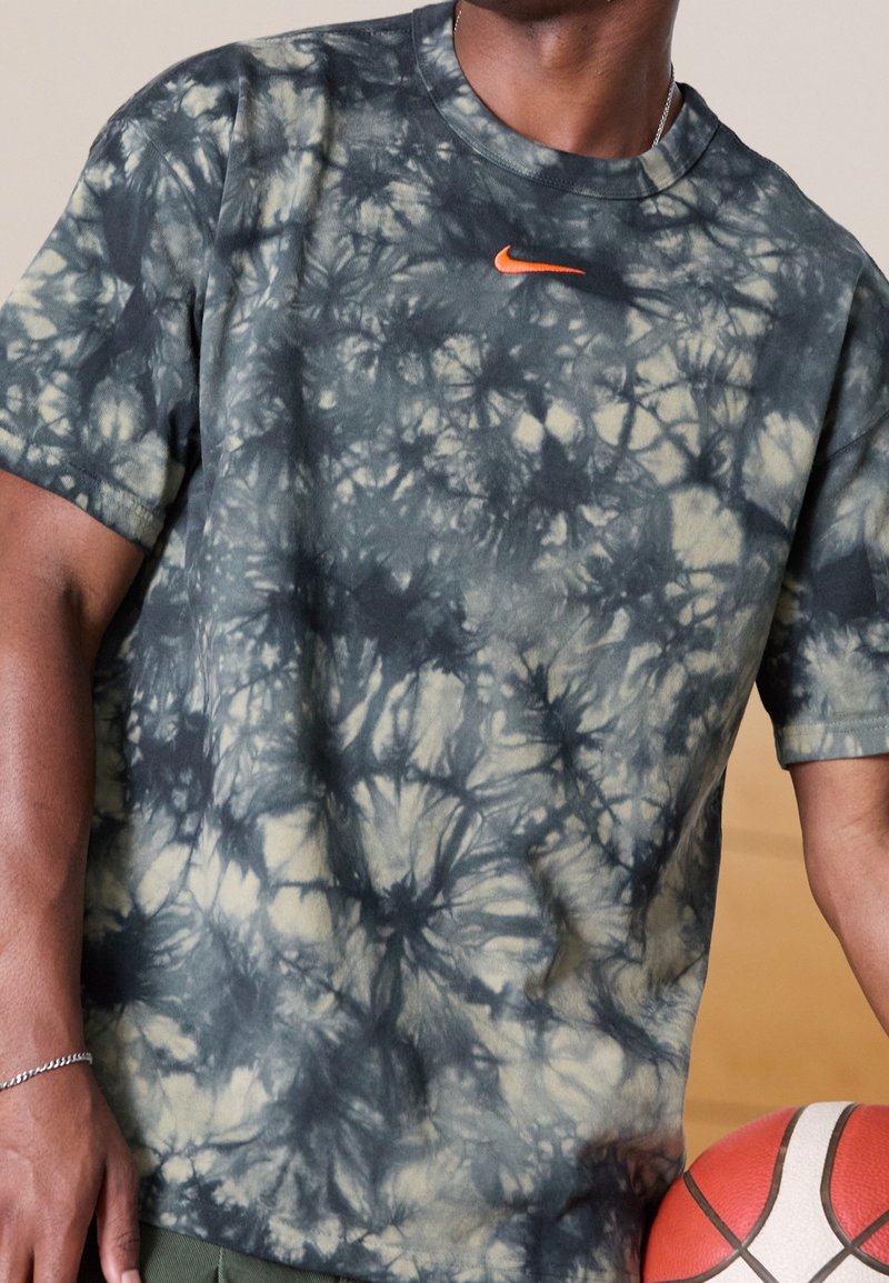 T-shirt Nike, manches courtes, motif tie-dye en vert et noir, logo orange sur la poitrine, tissu doux avec une coupe décontractée.