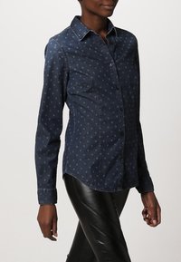 Jeansskjorta i mörkblått med ljusblå prickar, lång ärm, spetsig krage och framknäppning, med en figurnära passform och slät textur.