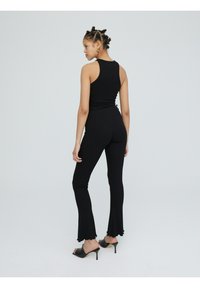 Zwarte geribbelde tanktop en flarepants set. Top heeft een racerback ontwerp, terwijl de broek een gegolfde zoom heeft. Draagt met open teen hakken.