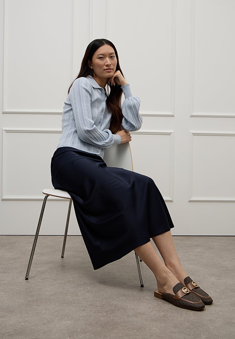 Lichtblauwe geribbelde gebreide blouse met kraag, gecombineerd met een donkerblauwe midi rok en bruine instappers met gouden accenten.