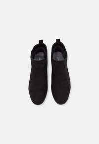 Botines de ante negro con un diseño minimalista, que cuentan con laterales elásticos y pequeñas lengüetas para facilitar su uso.