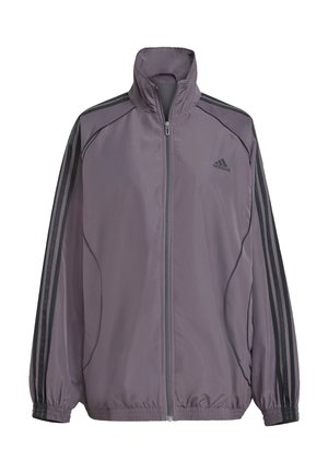 Vaaleanlila polyesteritakki, jossa on korkea kaulus, kokoontaitettava vetoketju, joustavat hihansuut ja kolme mustaa raitaa olkapäillä. Adidas-logo rinnassa.