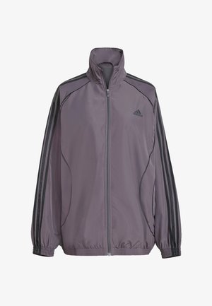 Svijetloplava poliester jakna s visokim ovratnikom, punim patentnim zatvaračem, elastičnim manžetama i tri crne pruge na ramenima. Adidas logo na prsima.