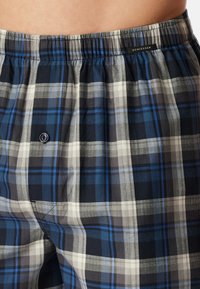 Boxers à carreaux pour homme en bleu marine, gris et bleu clair,avec une taille élastique et un seul bouton à l'avant. Texture de tissu en coton doux.