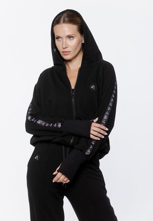Czarna bluza z kapturem na zamek, z dużym kapturem, prążkowanymi mankietami, naszywką z logo na piersi oraz wzorzystym wykończeniem na rękawach. Miękka tekstura materiału.