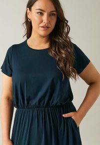 Granatowa sukienka o krótkim rękawie z marszczonym pasem, wykonana z gładkiego materiału. Ma okrągły dekold i boczne kieszenie dla większej praktyczności.