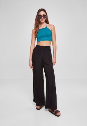 Turquoise crop top met smalle straps, gecombineerd met luchtige zwarte wijde pantalons. Model draagt donkere zonnebril en plateau sandalen.
