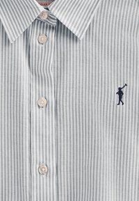 Camicia a maniche lunghe a righe in grigio chiaro e bianco, con colletto classico e logo ricamato in blu scuro. I dettagli dei bottoni sono beige.