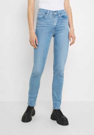Jeans ajustados de color azul claro hechos de mezclilla, con una altura media en la cintura, cinco bolsillos y costuras de contraste, combinados con botas negras gruesas.
