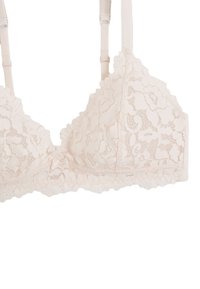 Bralette en dentelle de couleur pêche clair, avec des bords festonnés, des motifs floraux délicats, et un petit nœud au centre. Bretelles ajustables.