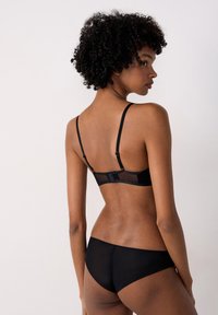 Schwarzes Lingerie-Set mit einem durchsichtigenMesh-Bralette mit verstellbaren Trägern und passenden schwarzen Panties, das glatte Texturen und ein minimalistisches Design betont.