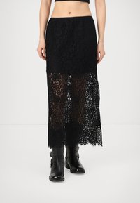 Fustă neagră din dantelă cu un model floral, partea inferioară transparentă și tiv ondulat, asortată cu cizme negre din piele până la genunchi. Talie elastică.