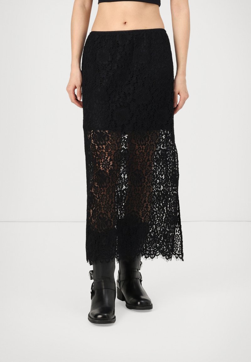 Fustă neagră din dantelă cu un model floral, partea inferioară transparentă și tiv ondulat, asortată cu cizme negre din piele până la genunchi. Talie elastică.