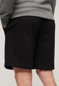 Shorts neri in cotone con cintura elastica, orli cuciti e tasche laterali. Il materiale sembra morbido e ha una texture liscia.