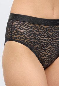 Διαφανές μαύρο εσώρουχο με λεοπάρ σχέδιο και ελαστική ζώνη με επώνυμο λογότυπο, φορεμένο στη χαμηλή λεκάνη και τα ισχία ενός ατόμου.