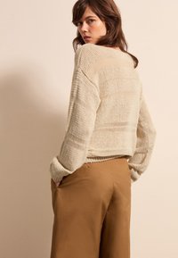 Beiger Strickpullover mit lockerer Passform und gerippten Bündchen, kombiniert mit braunen, hoch-taillierten Hosen. Strukturierten Stoff, entspanntes Design.