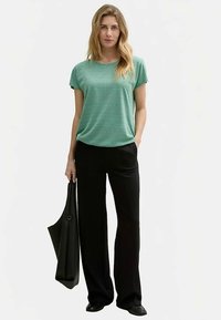 Zielona bluzka z krótkim rękawem o fakturowanym wzorze, zestawiona z czarnymi szerokimi spodniami i czarną torbą. Strój cechuje się luźnym krojem.