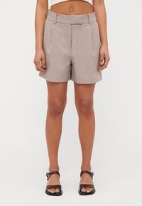 Shorts personalizați bej cu un model texturat, având un talie lată și două buzunare frontale, care se opresc deasupra genunchiului.