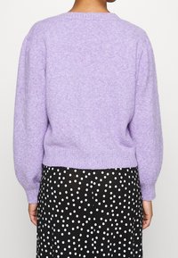 Lila gestrickter Pullover mit Ballonärmeln und geripptem Saum, kombiniert mit einem schwarzen Rock mit weißen Punkten. Weicher Stoff und lässiges Design.