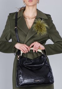 Mustas nahast käekott, millel on eesmine klapp, kuldne riistvara ja ülemine käepide. Kotil on tekstuuriga viimistlus ja eemaldatav rihm.