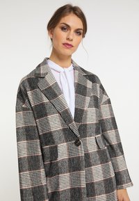 Blazer gri cu carouri, având un model îndrăzneț de pătrățele negre și albe, cu accente roșii, design dublu, și rever cu decupaj. Textură moale.